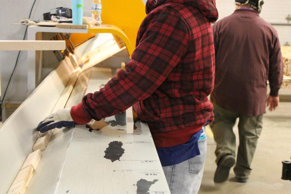 image of person holding a small strip of wood by a machine